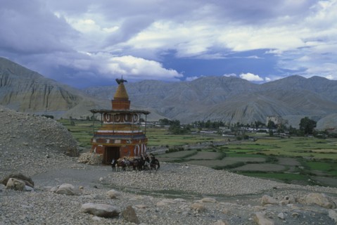 NEPAL, Mustang, Tsarang, Group of riders on ponies beside stupa marking the entrance to Tsarang.