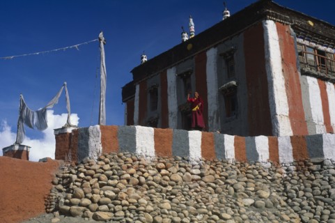 NEPAL, Mustang, Tsarang, Head monk looking out from terrace of temple painted with coloured stripes
