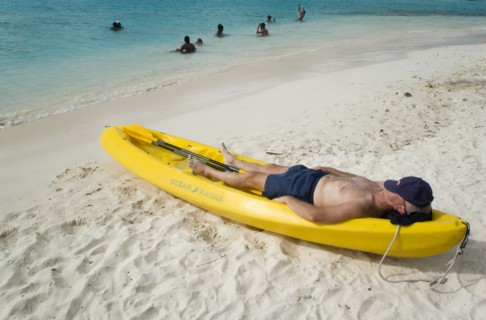 WEST INDIES, St Vincent & The Grenadines, Tobago Cays, Man lying in kayak sunbathing on the beach