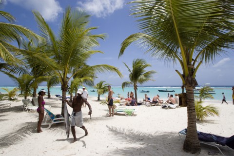 WEST INDIES, Barbados, Christ Church, Fisherman carrying gutted King Fish past tourists and coconut
