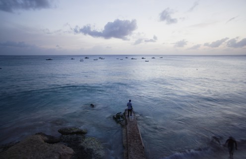 WEST INDIES, Barbados, St Lucy, Man on jetty at Half Moon Fort looking out to moored fishing boats