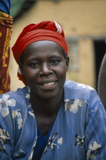 BURUNDI, Cibitoke District, Smiling woman sat with blue dress and red headscarf.