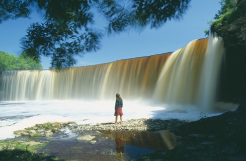 ESTONIA, Jagala, "Young woman standing in front of Jägala, steep horseshoe shaped waterfall between