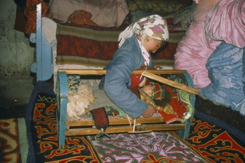 CHINA, Xinjiang Province, Kazakh woman breastfeeding baby in cot.