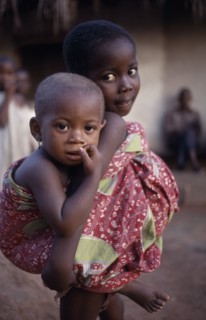 GHANA, Volta Region, Hohoe, Young girl looking after little sister carried on her back.