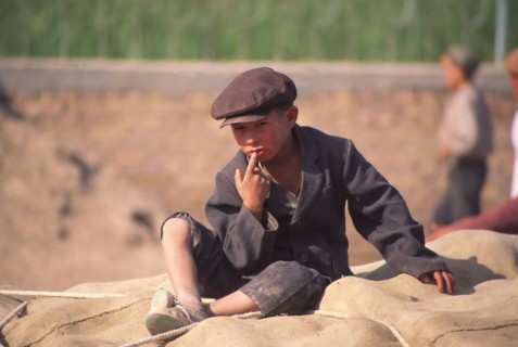 CHINA, Xinjiang Province, Kashgar,  Tajik boy sat on sacks