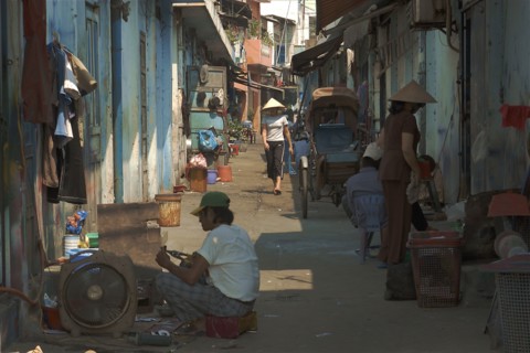 VIETNAM, South, Ho Chi Minh City, View down a side street with people sat on ground and a woman