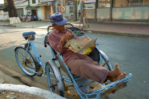 VIETNAM, South, Ho Chi Minh City, A Cyclo driver reading a magazine taking a break