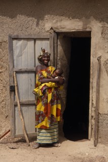MALI, People, Portrait of Malian mother and breastfeeding baby standing outside open doorway of mud