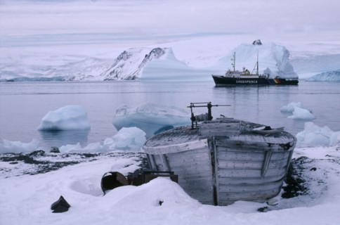 ANTARCTICA, King George Island, Old whale boat on land with Greenpeace ship in distance.