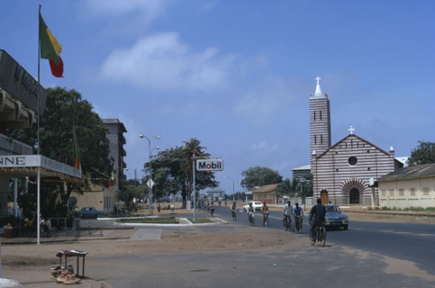BENIN, Cotonou, Street scene with church and passing cyclists and cars.