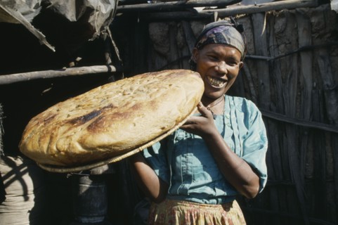 ETHIOPIA, Shoa Province, Nazareth, "Smiling woman holding up large, circular loaf of bread."