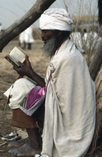 SUDAN, Religion, Amhara Ethiopian orthodox priest reading from book in refugee settlement.
