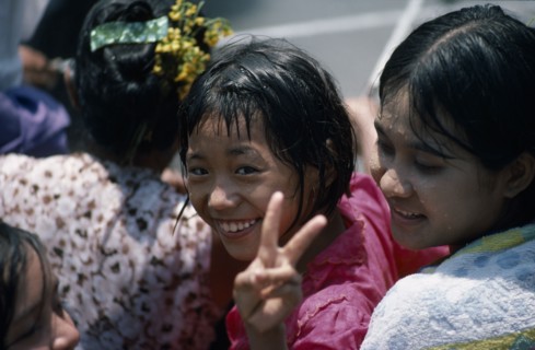 MYANMAR, Mandalay, Young girl smiling and making the V peace sign with fingers amongst other girls