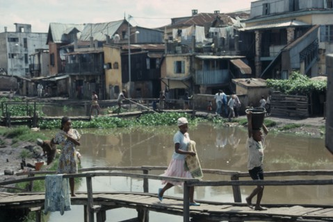 MADAGASCAR, Antananarivo, Children crossing wooden bridge over stagnant water in poor housing area