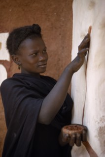 MAURITANIA, Oualata, Young woman decorating exterior wall of mud building with ochre.  It is