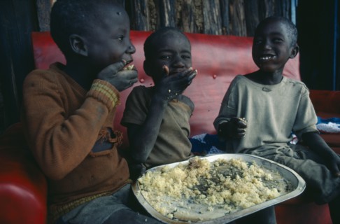KENYA, Children, Three young children using right hands to eat Christmas lunch.
