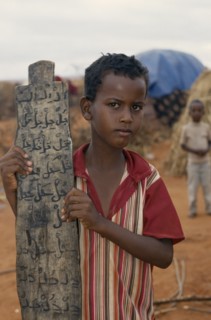 KENYA, Mandera, Somali refugee camp run by UNHCR.  Young boy attending Koranic school holding piece