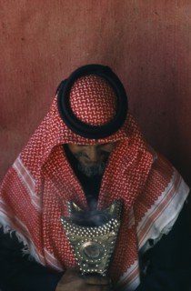 QATAR, Tribal People, Portrait of Bedouin man inside tent looking down at studded leather artefact.
