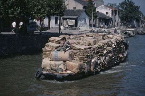 CHINA, Jiangsu Province, Suzhou, Man on boat travelling along the Grand Canal carrying piles of