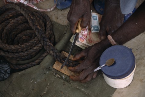 NIGERIA, Benue, Cropped shot of vendor cutting piece of tobacco at stall.