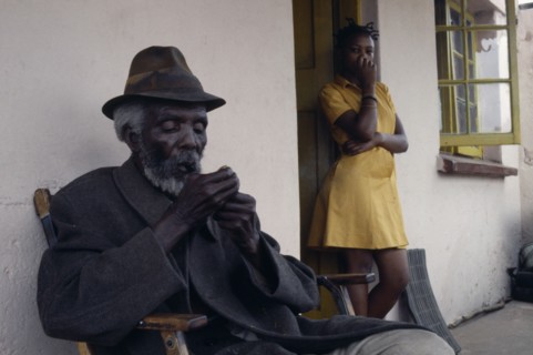 SOUTH AFRICA, Gauteng, Alexandra Township, Portrait of elderly seated man lighting pipe with girl