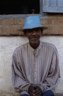 MADAGASCAR, Ihosy, Portrait of an elderly man sitting against a wall wearing a blue straw hat