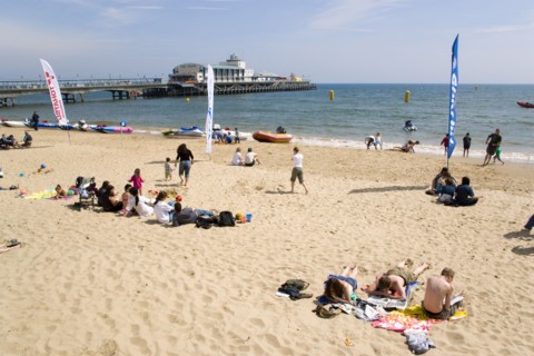 ENGLAND, Dorset, Bournemouth, Tourists on the sand of the West Beach beside the pier.