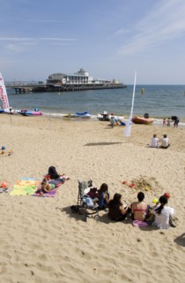 ENGLAND, Dorset, Bournemouth, Tourists on the sand of the West Beach beside the pier.