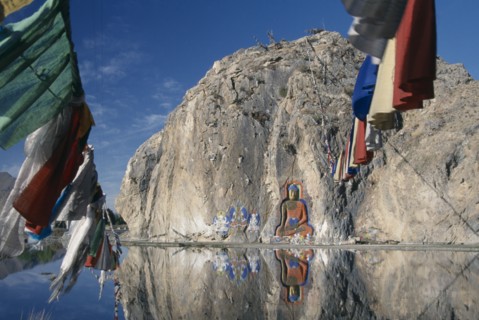 CHINA, Tibet, "Carved Buddha, Buddhist paintings and prayer flags on a rock wall by the road from