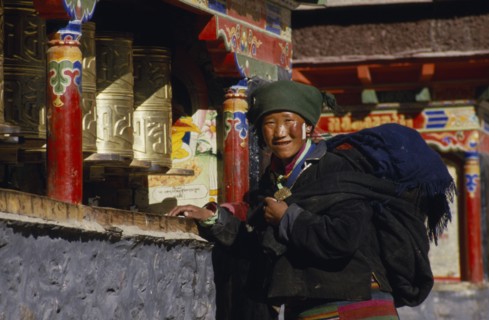 CHINA, Tibet, Sakya, A pilgrim turning prayer wheels outside the monastery.