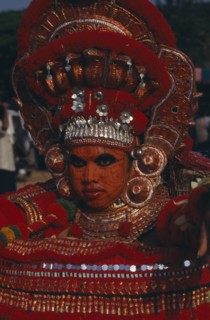 INDIA, Kerala, Thrissur, "Theyyam dancer in a red costume and painted face, at The Great Elephant