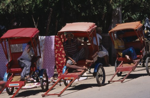 MADAGASCAR, Ambositra, Men drivers sitting in the shade of their Rickshaws waiting for a fare