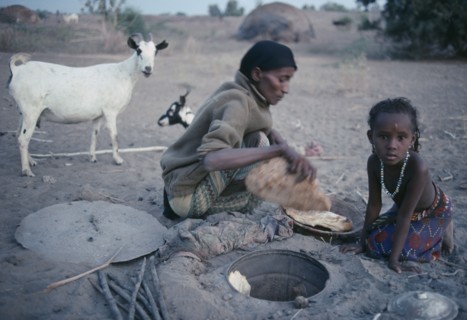 ETHIOPIA, North East, Afar tribeswoman baking bread in ground with child sitting beside her.