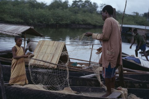 NIGERIA, Bonny, Fisherman and young girl untangling nets in wooden canoes.