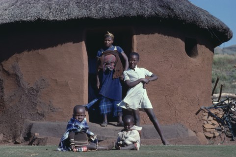 SOUTH AFRICA, Kwazulu Natal, "Mother and children in doorway of thatched, mud brick home."