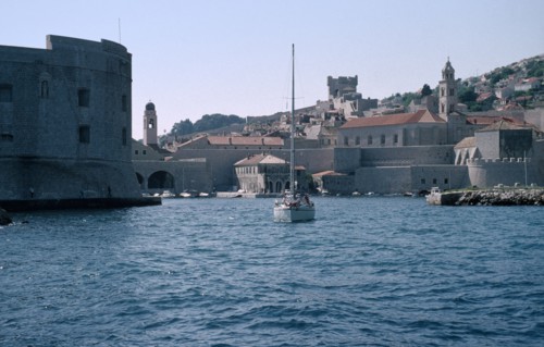 CROATIA, Dalmatia, Dubrovnik, The Old City harbour with stone fort and a yacht sailing on the water