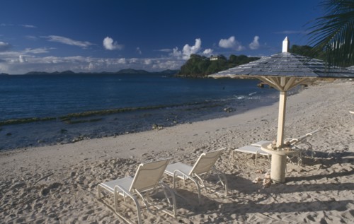 GRENADINES, Mustique, Endeavour Bay. Empty sun loungers on sandy beach with Bequia Island seen from
