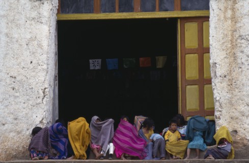 MEXICO, Chiapas, Children sitting in doorway of building wrapped in colourful blankets as