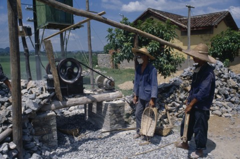 CHINA, Guangxi, Construction workers next to rock crushing machine.