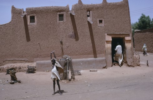 NIGERIA, Kano, Traditional mud Hausa dwelling with child standing with up-stretched arms outside
