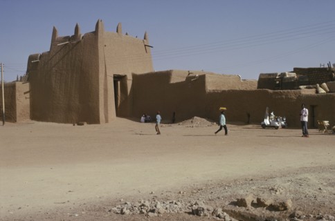 NIGERIA, Kano, Ancient mudbrick city walls and passing people and street trader carrying tray of