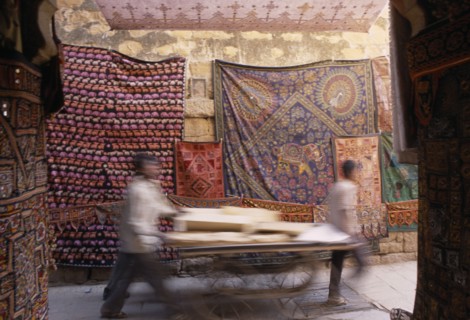 INDIA, Rajasthan, Jaisalmer, Jaisalmer Fort. Two men pushing a cart through a narrow street with
