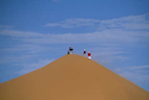 LIBYA, Sahara Desert, Tourists standing on top of Saharan sand dune.