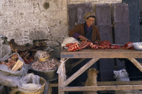 TIBET, Lhasa, Female vendor with yak meat for sale in Jokhang market.