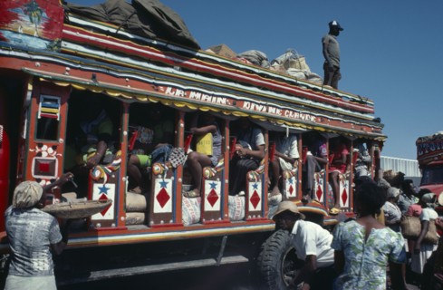 HAITI, Transport, Brightly painted and crowded taptap bus with waiting crowds and food sellers.