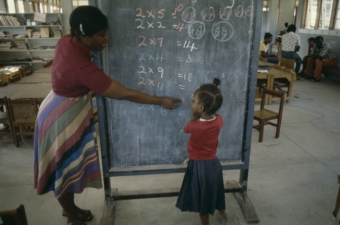GRENADA, Education, Female teacher pointing out 2 x table written in coloured chalk on blackboard