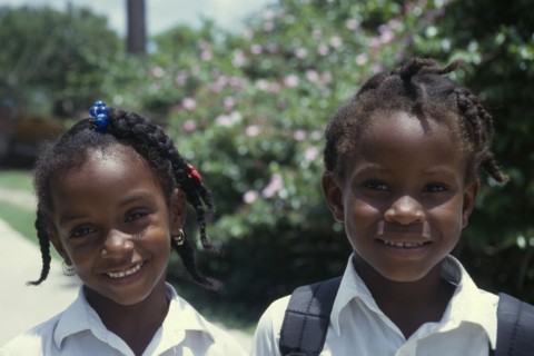 GRENADA, Petit Martinique, Head and shoulders portrait of two smiling schoolgirls with braided hair