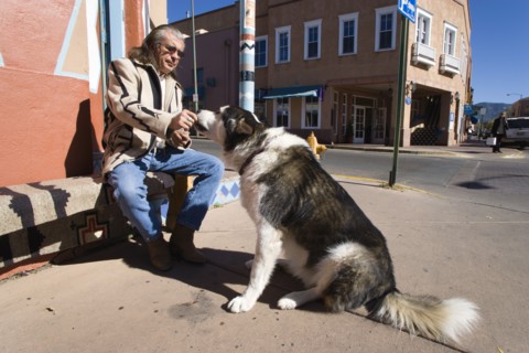 USA, New Mexico, Santa Fe, Native American man feeding his dog outside Father Sky Mother Earth