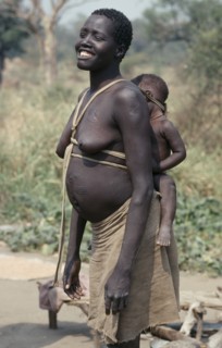 ETHIOPIA, West, Gambella, Uduk refugees from Sudan.  Smiling pregnant woman carrying baby on her